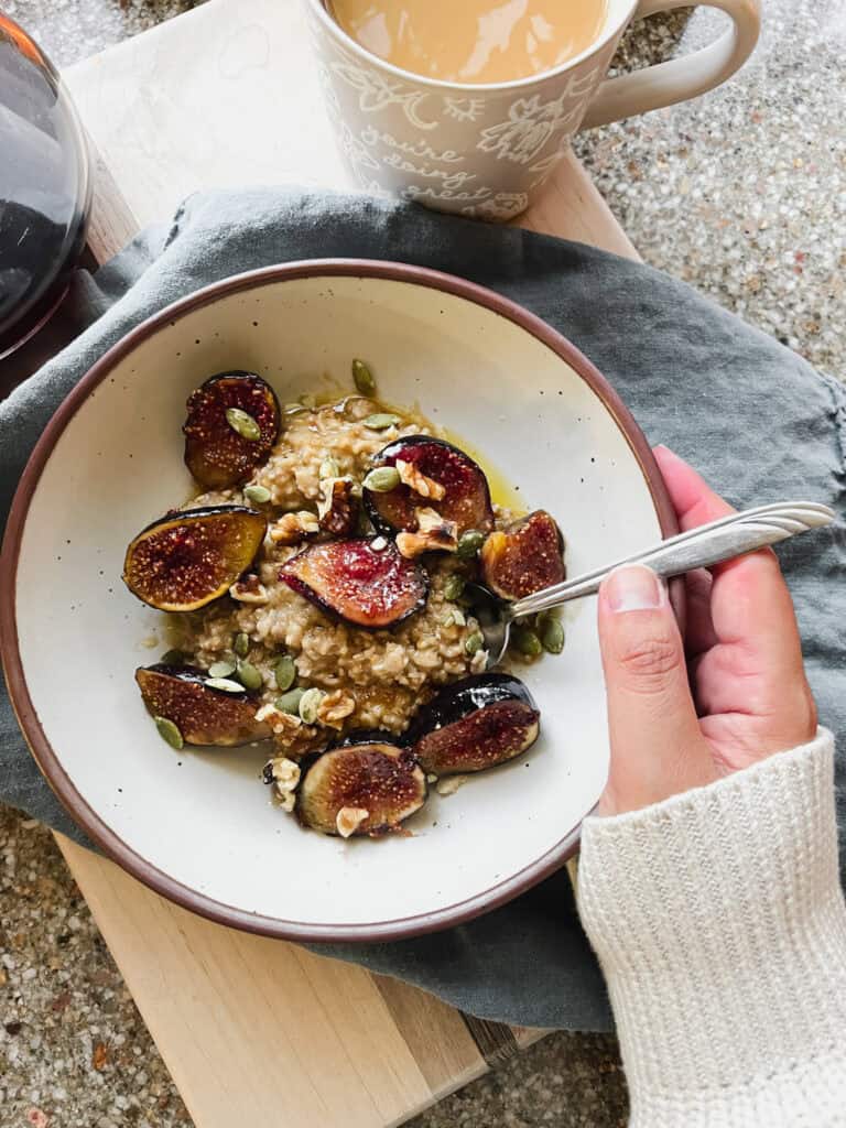 overhead photo of a woman's hand holding a bowl of oats topped with caramelized figs.